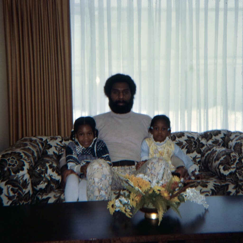 Digitized 1970s slide of Stephanie's dad on a floral sofa with his two young daughters, wearing his homemade floral pants