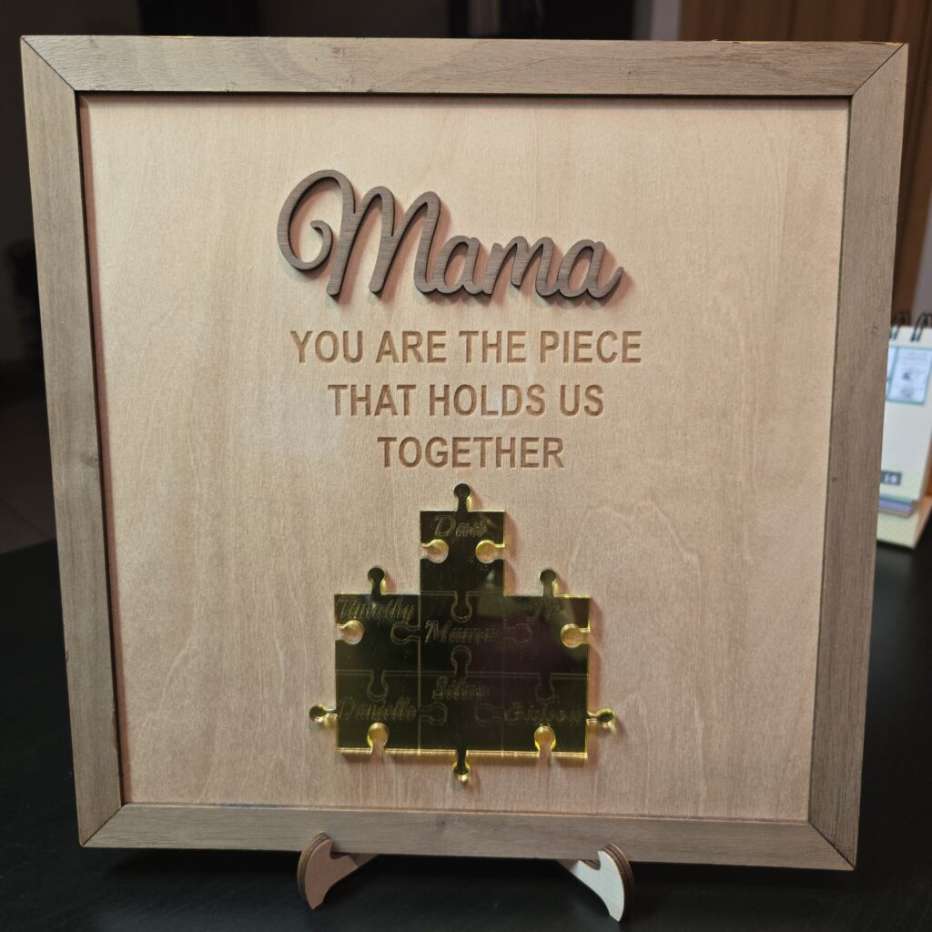 Framed wooden plaque reading "Mama, you are the piece that holds us together" with gold acrylic puzzle pieces engraved with each family member's name